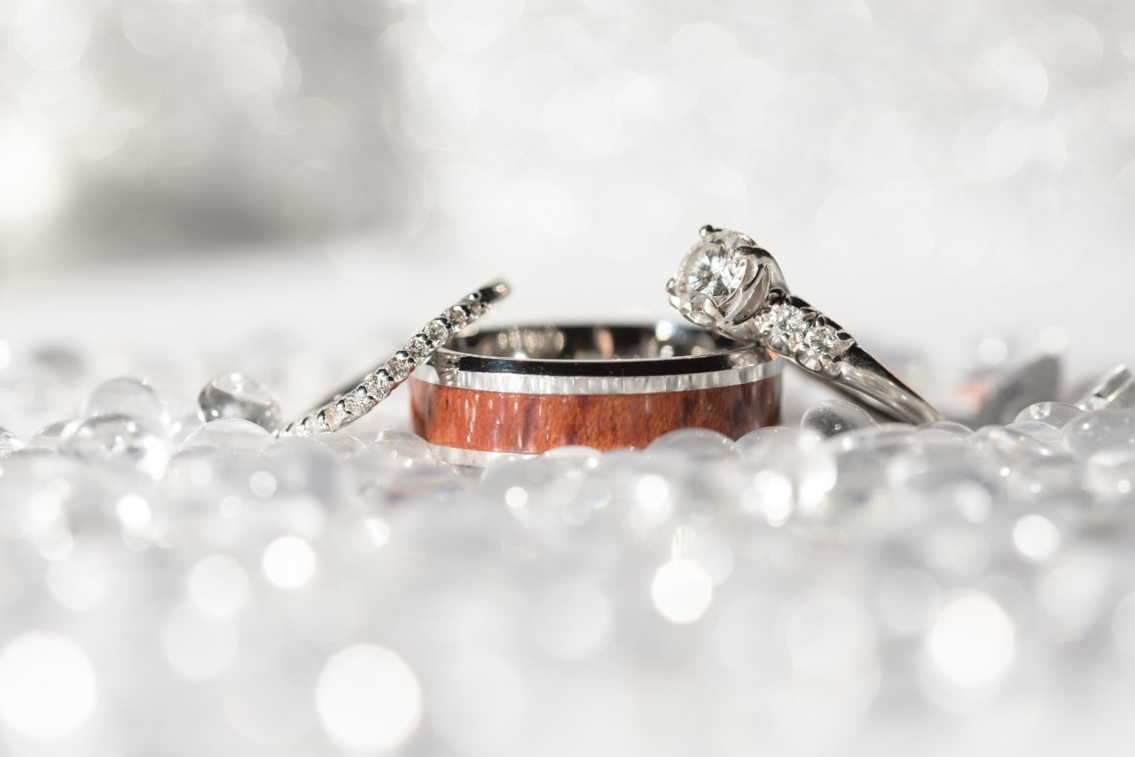 Trio of wedding rings, including a diamond engagement ring and a wooden band, surrounded by sparkling decorative crystals