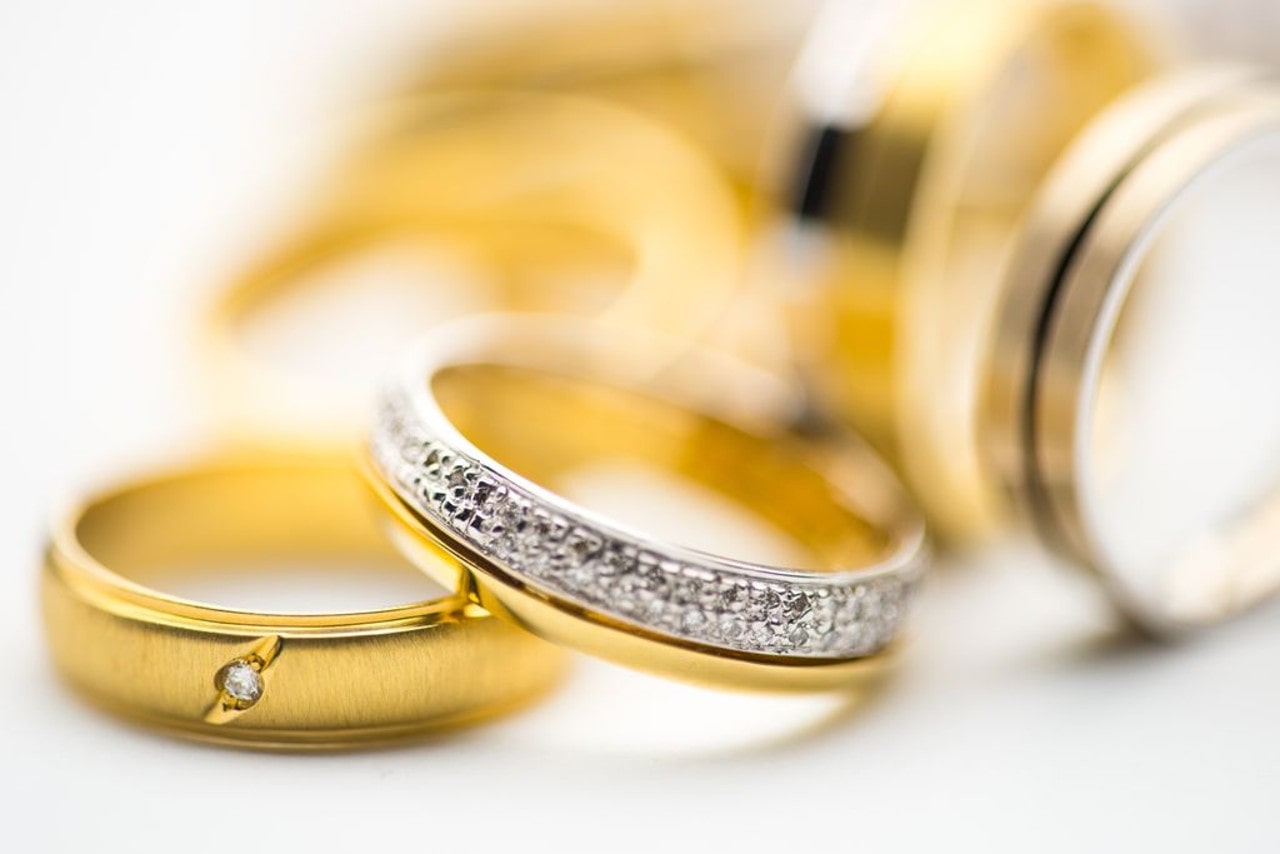 several gold wedding bands adorned with diamonds in the white background