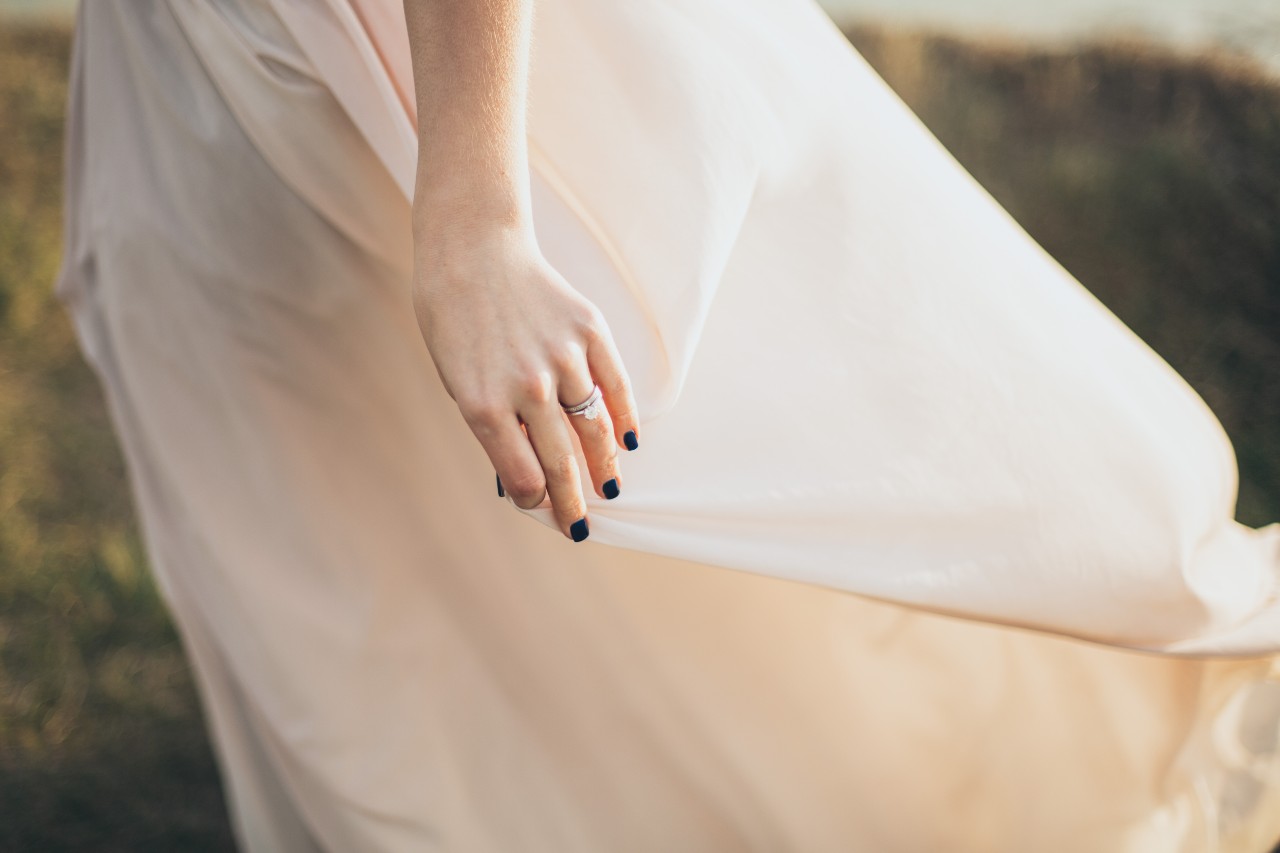 a bride walks through a field, holding her dress and wearing both bridal rings.