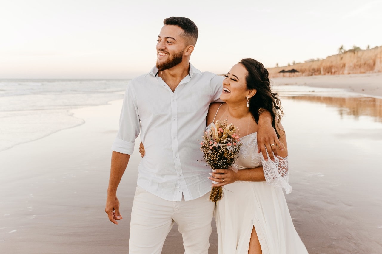 A newly married couple walks on a beach together.