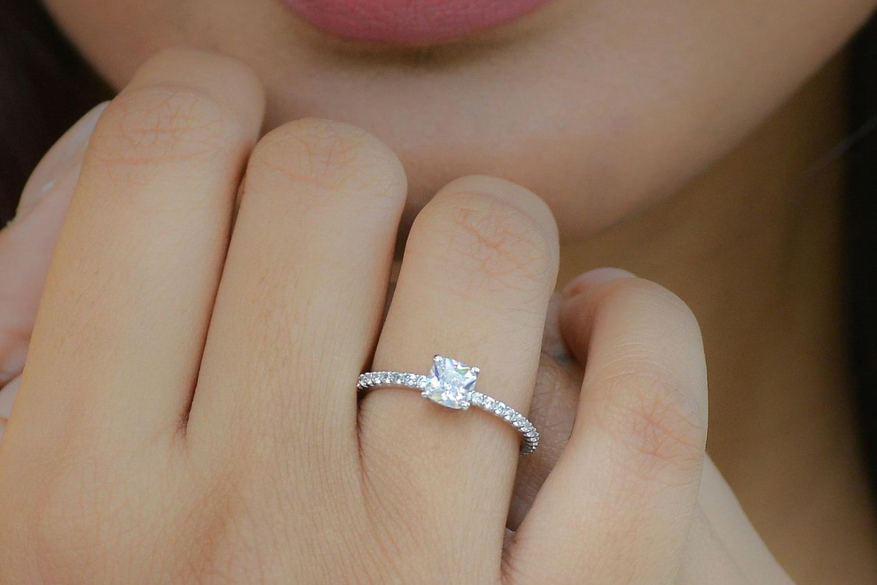 A closeup of a woman’s hand wearing a side stone engagement ring.