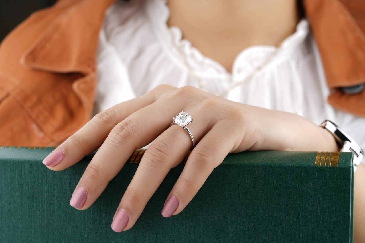 A woman holding a book wears a platinum solitaire engagement ring.