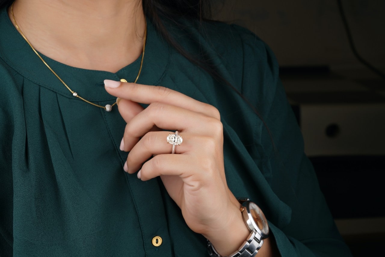 A woman adjusts her necklace wearing an oval cut diamond ring.