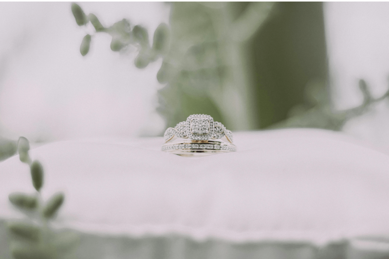 A distinctive engagement ring and wedding band displayed on a white pillow.